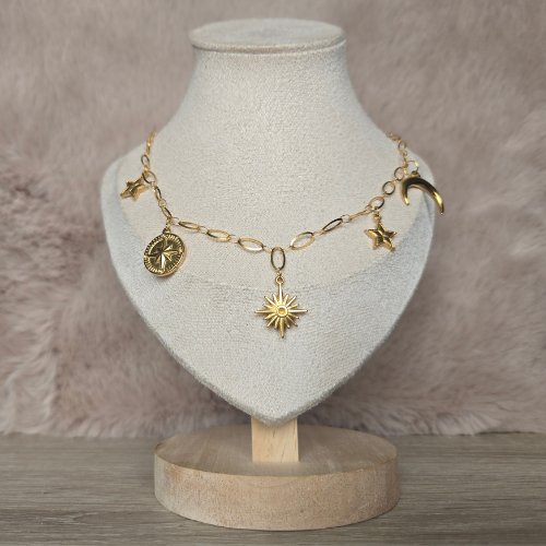 Handgemaakte gouden celestial ketting gepresenteerd op beige sieradenstandaard – met zon, maan en sterren bedels.