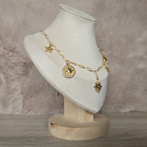 Close-up van gouden bedelketting met kompas en zon bedels – zijkantweergave op display standaard.