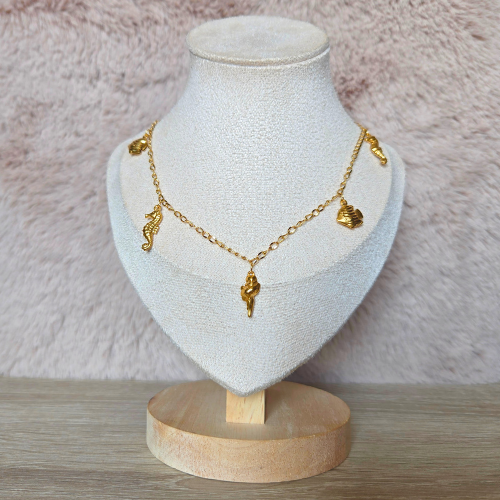Gouden zeethema ketting met bedels, gepresenteerd op een display standaard.