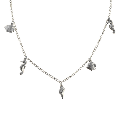 Zilverkleurige ketting met zeecharms zoals zeepaardjes, vissen en een schelp tegen een witte achtergrond.