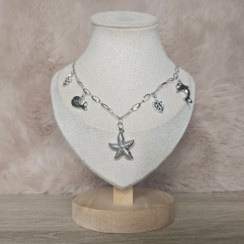 Zilverkleurige bedelketting met zeester, dolfijn, walvis en koraal bedels gepresenteerd op een sieradenstandaard.