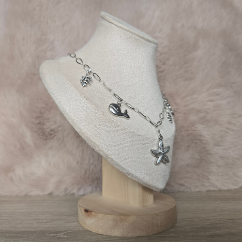 Zijaanzicht van een zilverkleurige oceaan bedelketting met zeedieren, gepresenteerd op een fluwelen display.