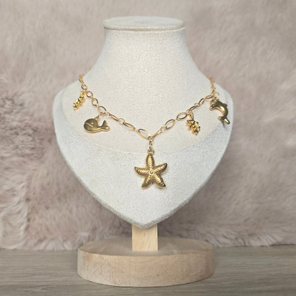 Handgemaakte goudkleurige ketting met zeethema op sieradendisplay, inclusief dolfijn-, walvis-, zeester- en koraalbedels.