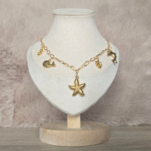 Handgemaakte goudkleurige ketting met zeethema op sieradendisplay, inclusief dolfijn-, walvis-, zeester- en koraalbedels.