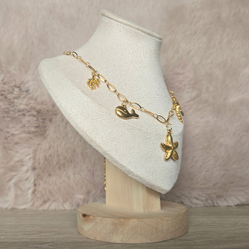 Zomerse goudkleurige bedelketting met oceaanfiguren, gefotografeerd vanaf de linkerkant op een sieradendisplay.