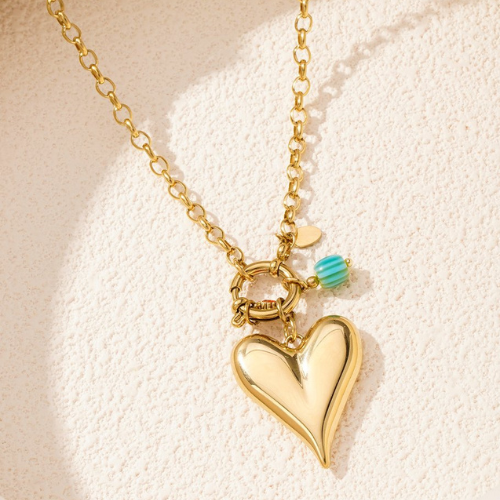Goudkleurige Brielle Ketting met grote hartvormige hanger, turquoise kraal en roodkleurig detail in de zon