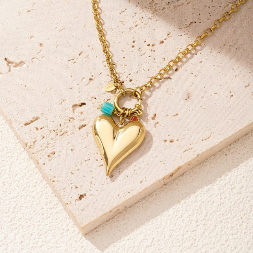 Goudkleurige Brielle Ketting met grote hartvormige hanger, turquoise kraal en goudkleurig detail in de zon op een stenen ondergrond