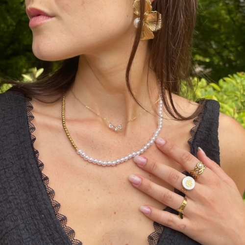 Goudkleurige ketting met drie aaneengesloten zirkonia hartjes om de hals gedragen en gecombineerd met een parelketting