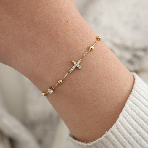 Stijlvol goudkleurige armband met een elegant kruisje en glinsterende zirkonia steentjes gedragen om de pols – van roestvrij staal