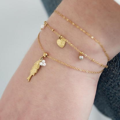 Goudkleurige Fishy Armband met visbedel en pareltjes – gelayered met andere minimalistische armbanden
