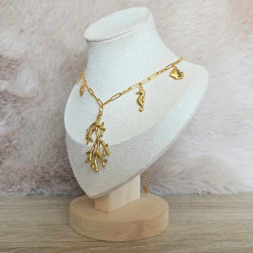 Zijdelingse weergave van een gouden bedelketting met oceaanbedels op een sieradenstandaard.