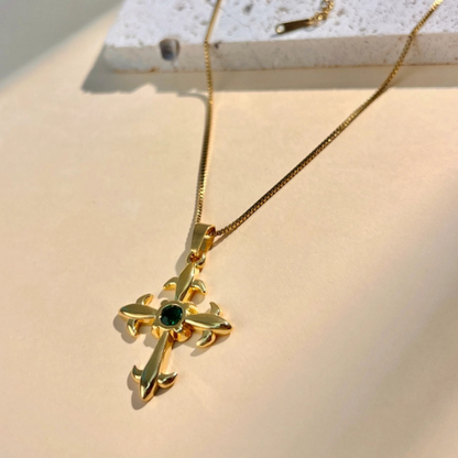 Goudkleurige kruis ketting met groene steen in het zonlicht