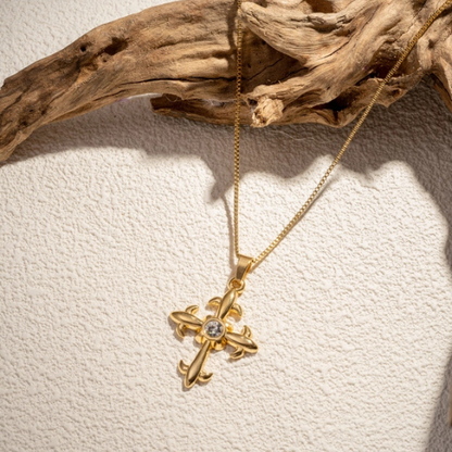 Goudkleurige kruis ketting met zirkonia steen in het zonlicht