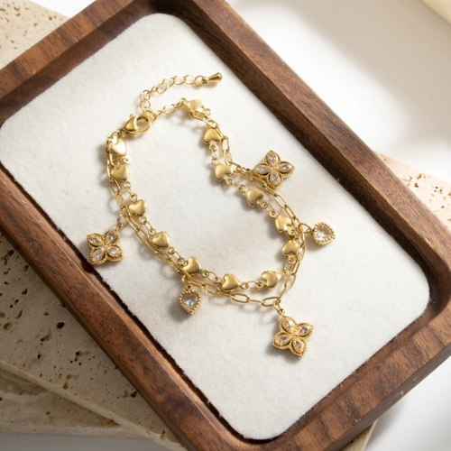 Goudkleurige dubbele armband met hartjes, schakels, zirkonia klavers en hartjes op een tray in het licht