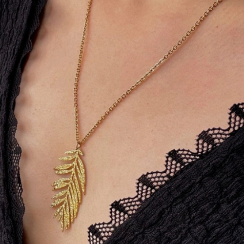 Goudkleurige ketting met blad van bovengemiddelde lengte gedragen om de hals 
