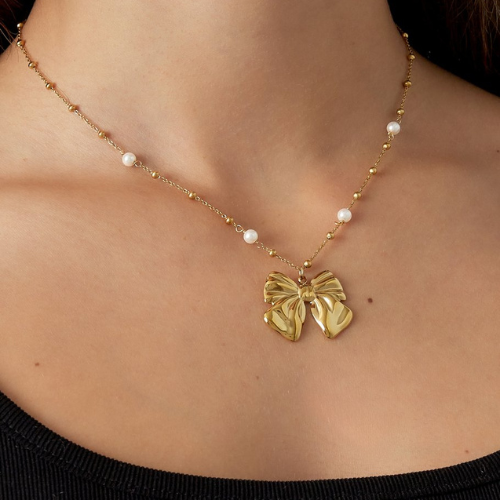 Goudkleurige parelketting met elegante strikhanger en subtiele pareldetails - om de hals gedragen