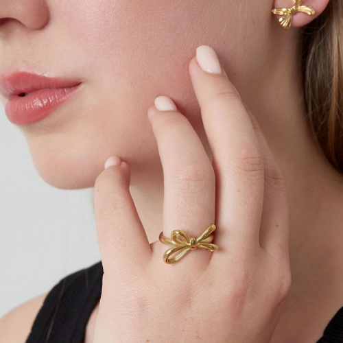 Vrouw draagt een goudkleurige strikring aan haar vinger – elegante en verfijnde sieradenstijl met een speelse touch.
