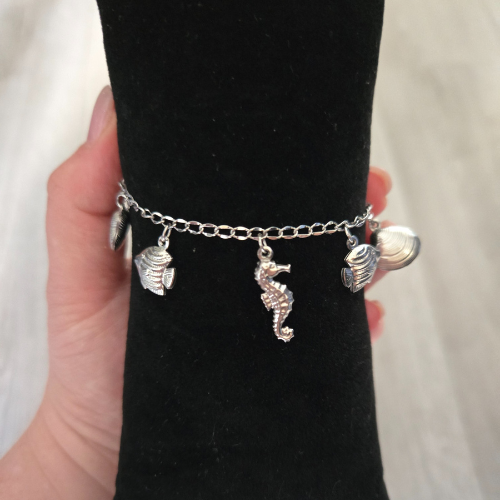 Handgemaakte bedelarmband van roestvrijstaal met zomerse bedels - ideaal voor op vakantie - op een sieradenkussentje